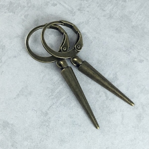 May include: A pair of bronze-colored earrings with a pointed design. The earrings are made of metal and have a hoop design.