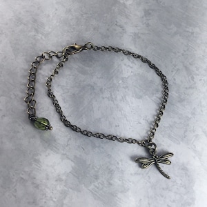 May include: A delicate bronze chain bracelet with a dragonfly charm and a green glass bead.