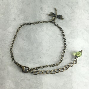 May include: A delicate bronze chain bracelet with a dragonfly charm and a green crystal bead.