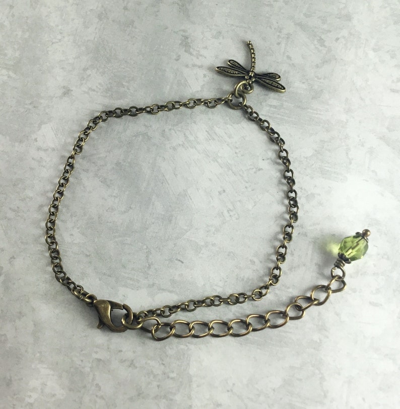 May include: A delicate bronze chain bracelet with a dragonfly charm and a green crystal bead.