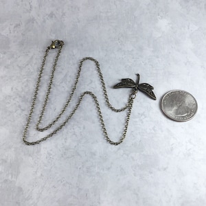 Peut inclure: Un collier en cha&icirc;ne bronze avec un pendentif en forme de libellule. Le pendentif est d&eacute;taill&eacute; et complexe, avec des ailes d&eacute;licates et un corps long et fin. La cha&icirc;ne est une cha&icirc;ne simple et li&eacute;e.