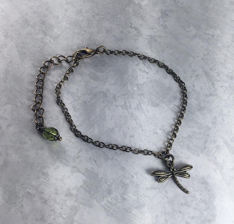 Peut inclure: Un bracelet d&eacute;licat en cha&icirc;ne bronze avec un pendentif en forme de libellule et une perle de verre verte. Le bracelet est r&eacute;glable et poss&egrave;de un fermoir &agrave; mousqueton.