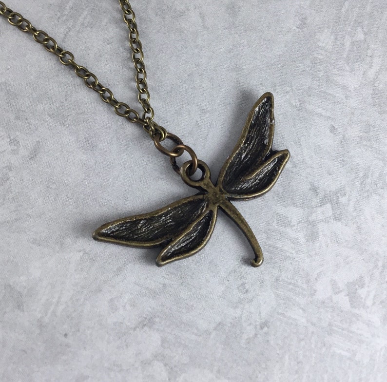 Peut inclure: Un collier avec un pendentif en forme de libellule en bronze sur une cha&icirc;ne d&eacute;licate.