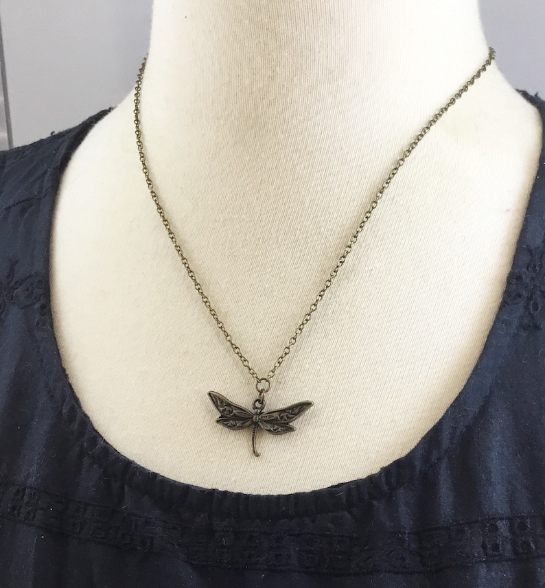 Peut inclure: Un collier en cha&icirc;ne bronze avec un pendentif en forme de libellule d&eacute;taill&eacute;.