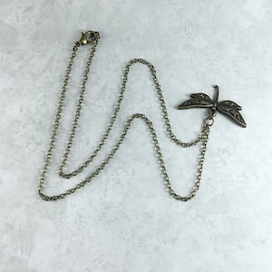 Peut inclure: Un collier en cha&icirc;ne bronze avec un pendentif d&eacute;licat en forme de libellule. La libellule pr&eacute;sente des d&eacute;tails complexes et une finition l&eacute;g&egrave;rement oxyd&eacute;e.
