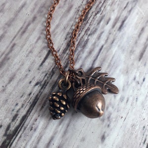 May include: A copper necklace with a charm featuring an acorn, a pinecone, and an oak leaf.