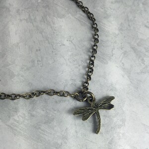 May include: A bronze chain necklace with a dragonfly pendant. The dragonfly is detailed and has a textured finish.