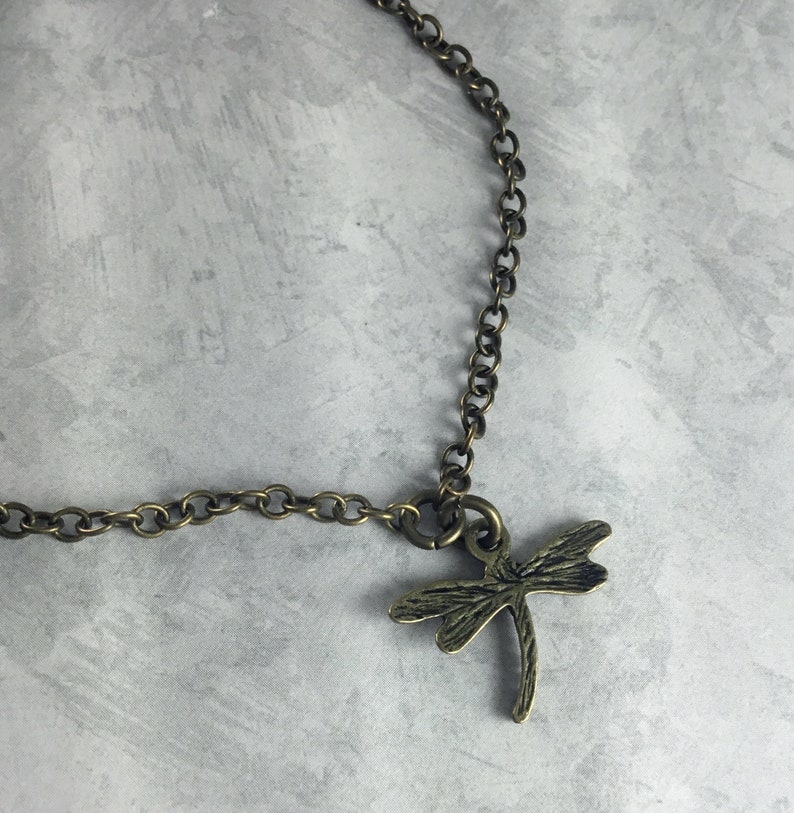 May include: A bronze chain necklace with a dragonfly pendant. The dragonfly is detailed and has a textured finish.