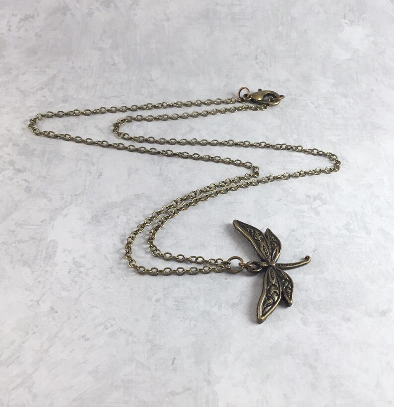 Peut inclure: Un collier en cha&icirc;ne bronze avec un pendentif en forme de libellule d&eacute;taill&eacute;.