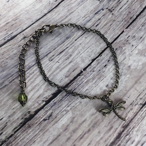 May include: A bronze chain bracelet with a dragonfly charm and a green glass bead. The bracelet has an adjustable clasp.