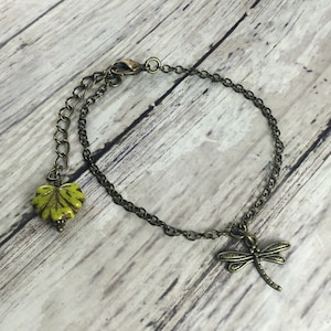 May include: A bronze chain bracelet with a green leaf charm and a dragonfly charm.