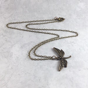 May include: A delicate gold chain necklace featuring a detailed dragonfly pendant. The dragonfly is intricately designed with filigree details.