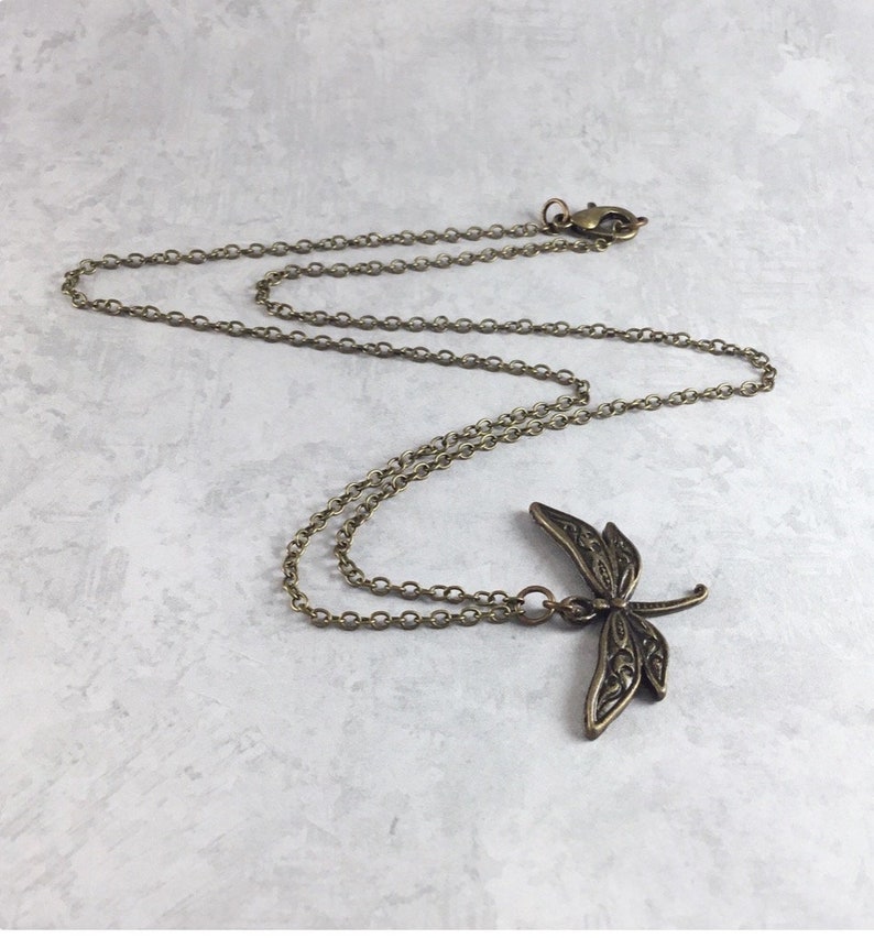 May include: A delicate gold chain necklace featuring a detailed dragonfly pendant. The dragonfly is intricately designed with filigree details.