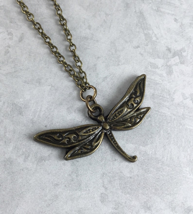 Peut inclure: Un collier avec un pendentif en forme de libellule en bronze avec un design complexe. La cha&icirc;ne est &eacute;galement en bronze.
