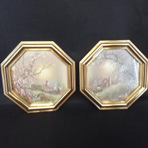 May include: Two framed landscape prints with gold octagonal frames. The prints depict a rural scene with a building, trees, and a soft, diffused light. The frames have a gold finish, adding a touch of elegance to the artwork.