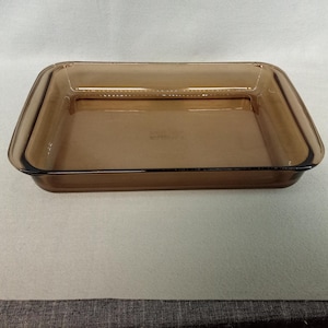 May include: A rectangular, amber-colored glass baking dish. The dish has a simple, classic design with slightly rounded corners and a smooth surface. The glass is transparent, allowing visibility of the contents. A practical kitchenware item.