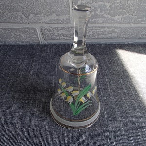 May include: A clear glass bell with a gold trim and a painted design of white lilies with green leaves.