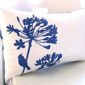 May include: White pillow with a blue floral design and a small bird silhouette. The flowers are stylized and resemble a cluster of blossoms.