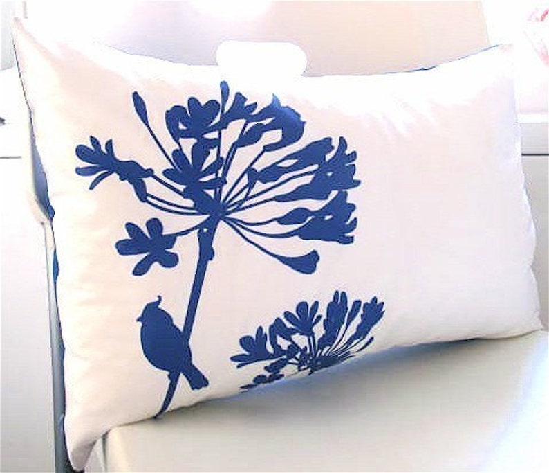 May include: White pillow with a blue floral design and a small bird silhouette. The flowers are stylized and resemble a cluster of blossoms.