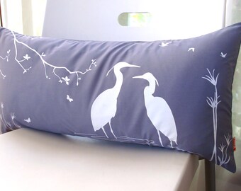 Puede incluir: Una almohada gris con una silueta blanca de dos pájaros y una rama con hojas. La almohada está sobre una superficie blanca.