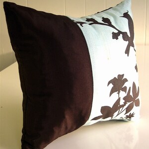 K&ouml;nnte beinhalten: Ein braunes und hellblaues Kissen mit Blumendesign. Das Kissen hat eine braune Seite und eine hellblaue Seite mit einem schwarzen Blumendesign.