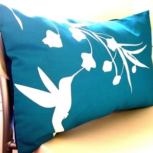Puede incluir: Almohada de tiro azul turquesa con una silueta blanca de un colibr&iacute; y flores.