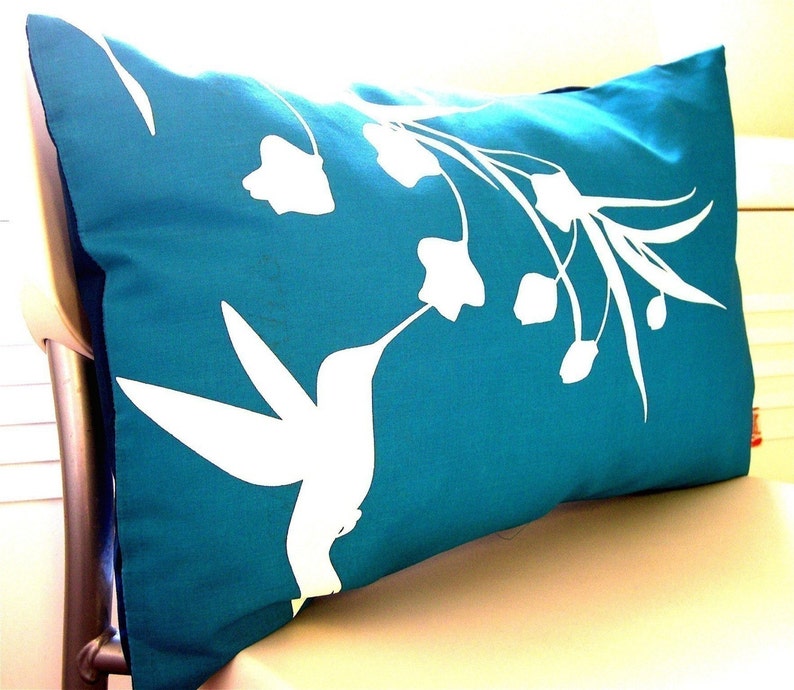 Puede incluir: Almohada de tiro azul turquesa con una silueta blanca de un colibr&iacute; y flores.