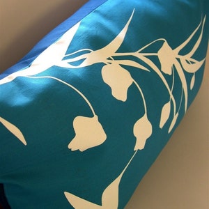 Puede incluir: Una almohada azul turquesa con un dise&ntilde;o floral blanco. Las flores son estilizadas y tienen un aspecto simple y moderno.
