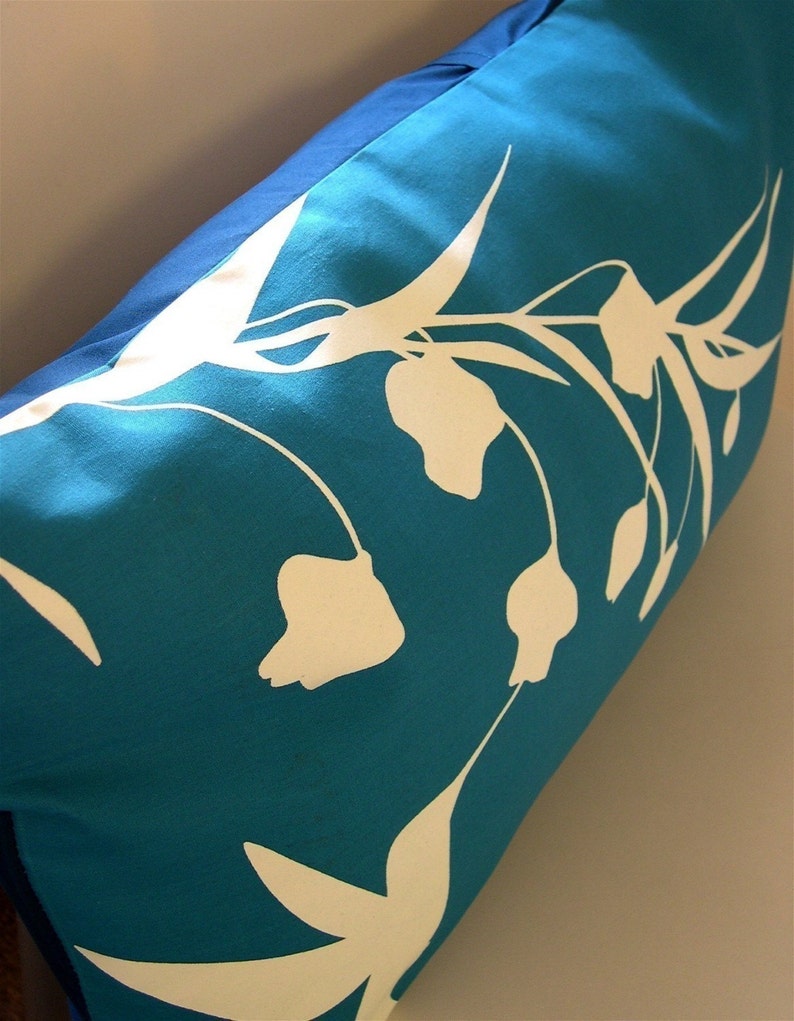 Puede incluir: Una almohada azul turquesa con un dise&ntilde;o floral blanco. Las flores son estilizadas y tienen un aspecto simple y moderno.