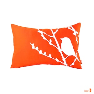May include: Orange throw pillow with a white silhouette of a bird on a branch.