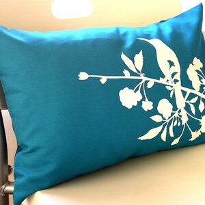 May include: A teal blue pillow with a white silhouette of a bird perched on a branch with flowers.