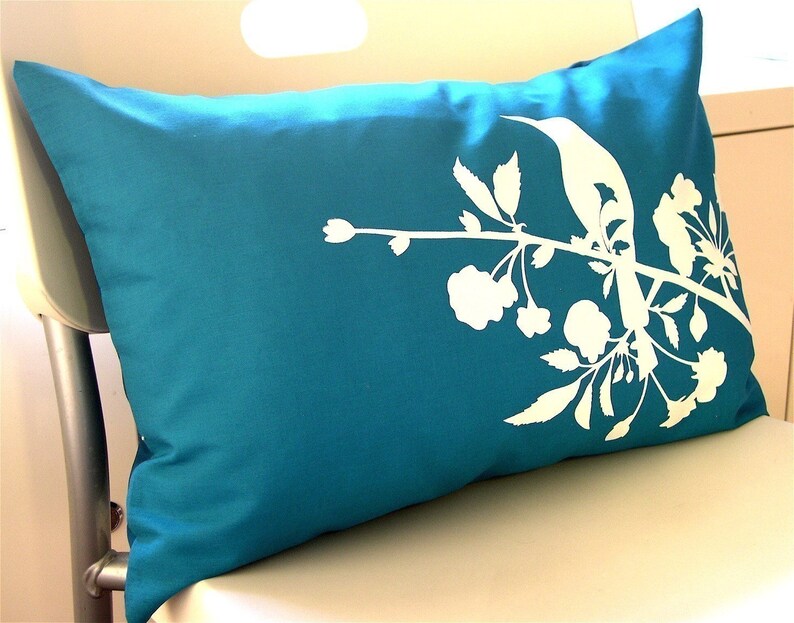 May include: A teal blue pillow with a white silhouette of a bird perched on a branch with flowers.