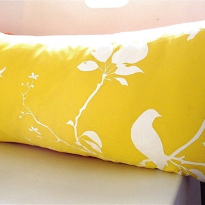May include: A yellow throw pillow with a white silhouette design of birds and branches.