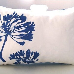 May include: White pillow with a blue silhouette of a flower and a bird. The flower has a large, round head with many petals. The bird is perched on a branch of the flower.