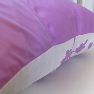 May include: A purple pillow with a white border and a floral design. The pillow is made of a soft, silky material.