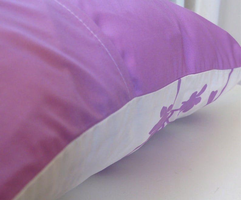 May include: A purple pillow with a white border and a floral design. The pillow is made of a soft, silky material.