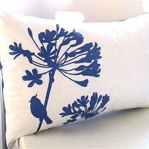 May include: White pillow with a blue silhouette of a flower and a bird. The flower has a long stem and many petals. The bird is perched on the stem.