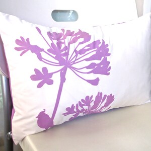 May include: A white pillow with a purple floral design. The pillow features a large flower with a stem and leaves, and a smaller flower in the bottom right corner.