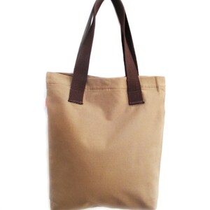 Op de afbeelding: Een bruine canvas tote bag met bruine hengsels. De tas is leeg.