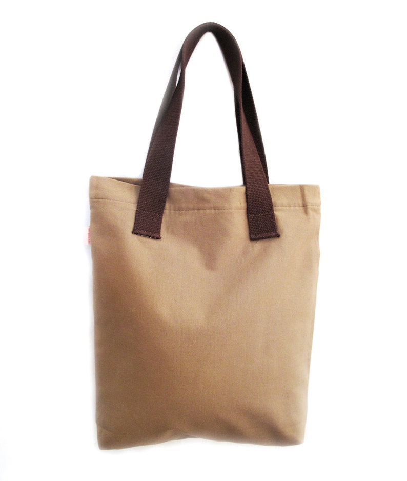 Op de afbeelding: Een bruine canvas tote bag met bruine hengsels. De tas is leeg.