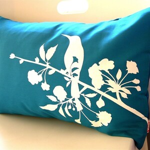 May include: Teal blue throw pillow with a white silhouette of a bird perched on a branch with white flowers.