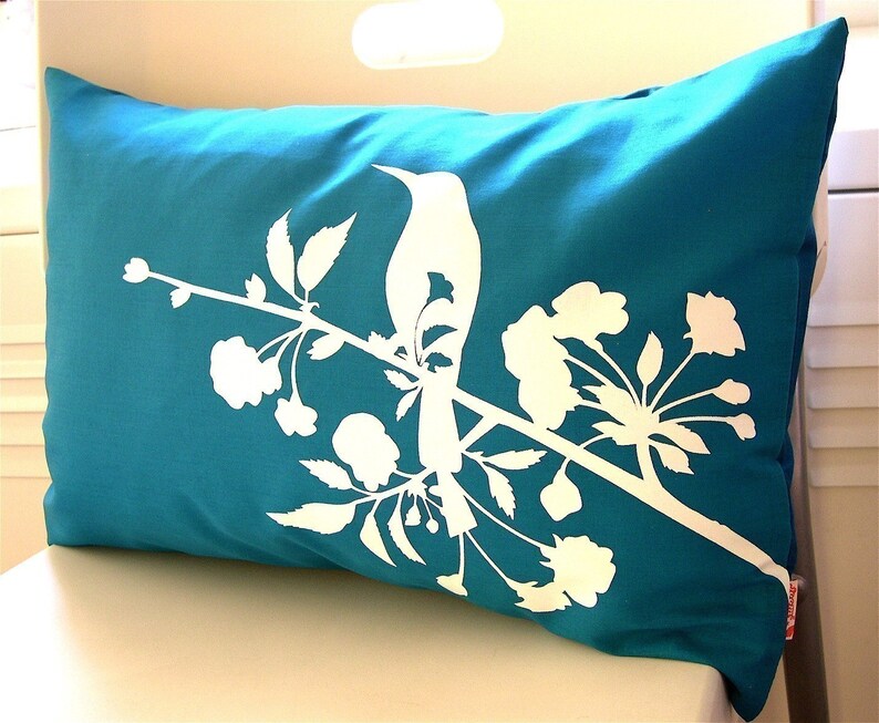 May include: Teal blue throw pillow with a white silhouette of a bird perched on a branch with white flowers.