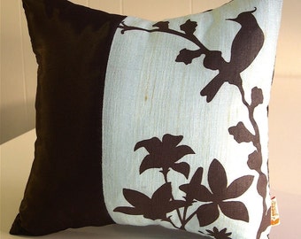 May include: A decorative pillow with a brown and blue design. The pillow features a silhouette of a bird and flowers on a light blue background. The other side of the pillow is solid brown.
