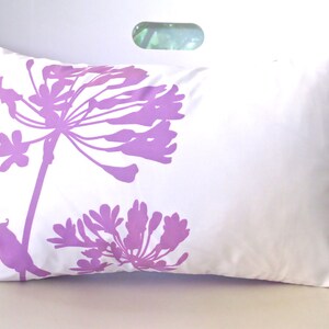 May include: White pillow with a purple floral design. The design features two large flowers and a small bird.
