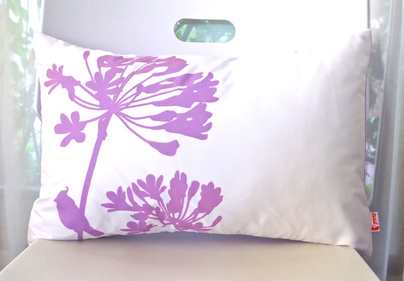 May include: White pillow with a purple floral design. The design features two large flowers and a small bird.