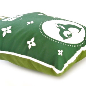 May include: Green pillow with a white outline and white floral designs. The center of the pillow features a white circle with a stylized white animal inside.