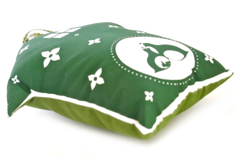 May include: Green pillow with a white outline and white floral designs. The center of the pillow features a white circle with a stylized white animal inside.