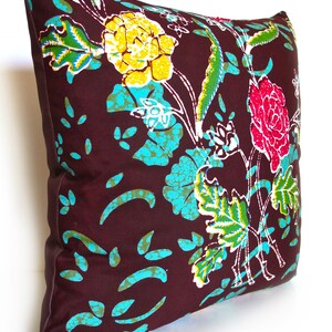 May include: A brown pillow with a floral pattern in shades of yellow, turquoise, green, pink, and white. The pillow has a white border.
