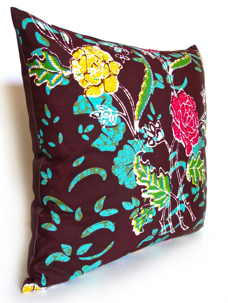 May include: A brown pillow with a floral pattern in shades of yellow, turquoise, green, pink, and white. The pillow has a white border.