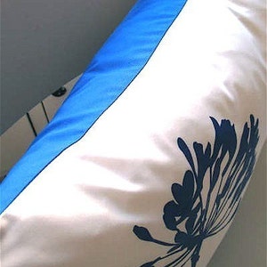 May include: A white pillow with a blue border and a blue floral design. The pillow is made of a soft, smooth fabric.